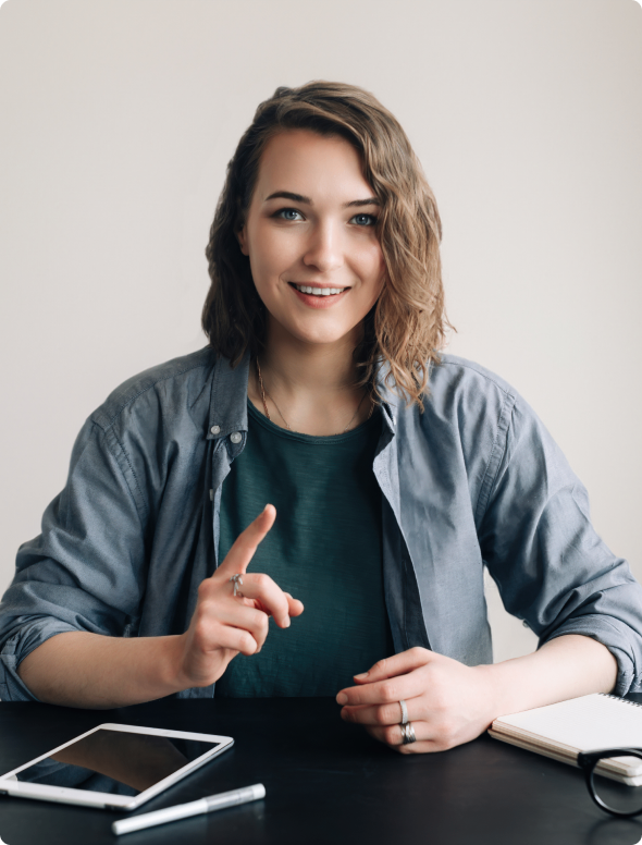 GettyImages-1499503574 Smiling person gesturing at desk with tablet.