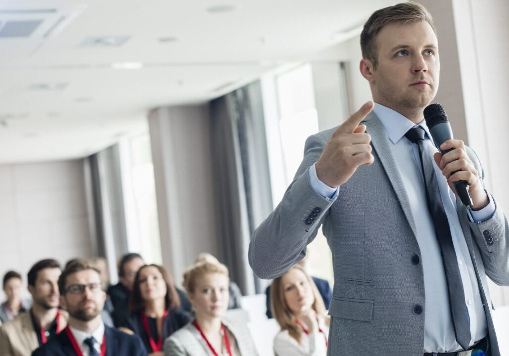 Man speaking at a conference with microphone.
